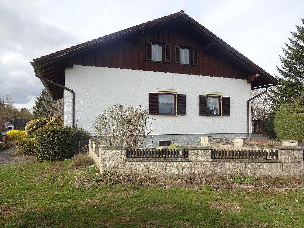 Rückansicht des Hauses mit Satteldach, weißer Fassade und einer niedrigen Steinmauer im Gartenbereich.