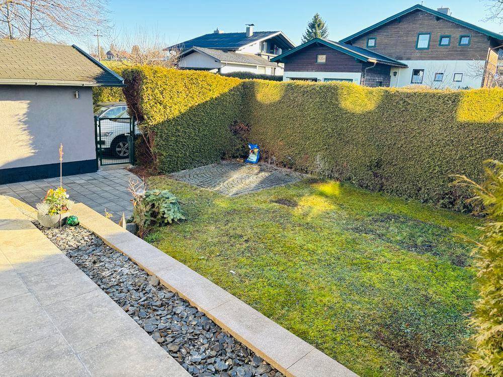 Gepflegter Gartenbereich mit Rasenfläche und hoher Hecke, umgeben von weiteren Häusern.