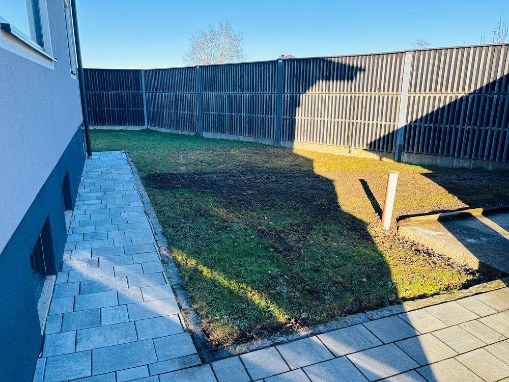 Hinterer Gartenbereich mit Rasen, gepflastertem Weg und hohem Sichtschutzzaun.
