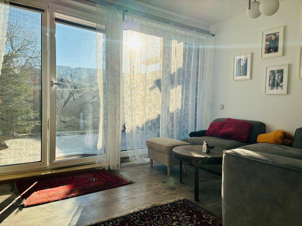 Lichtdurchfluteter Wohnbereich mit großen Fenstern, Zugang zur Terrasse und gemütlichem Sofa.