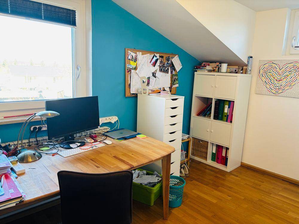 Helles Arbeitszimmer mit Schreibtisch, Regal und farbiger Akzentwand unter Dachschräge.