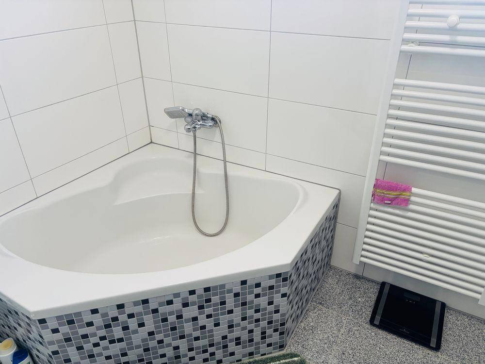 Eckbadewanne mit dekorativen Mosaikfliesen und einem praktischen beheizten Handtuchhalter.