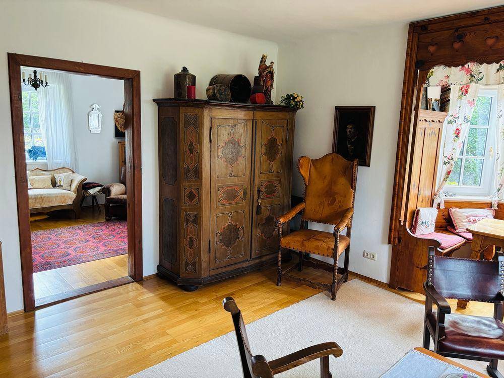 Geräumiges Wohnzimmer mit antiken Holzmöbeln, Holzboden und Zugang zu einem weiteren Raum.