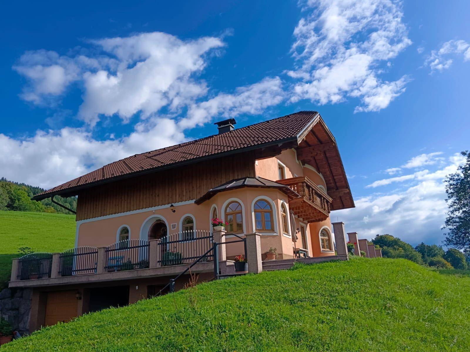 Attraktives Landhaus mit orangefarbener Fassade und Holzbalkon, auf einem Hügel gelegen mit weitem Blick.
