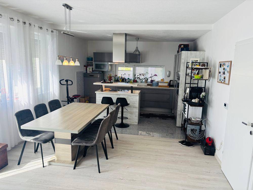 Moderner Essbereich mit großem Tisch und offener Verbindung zur Küche, inklusive Kücheninsel mit Barhockern.
