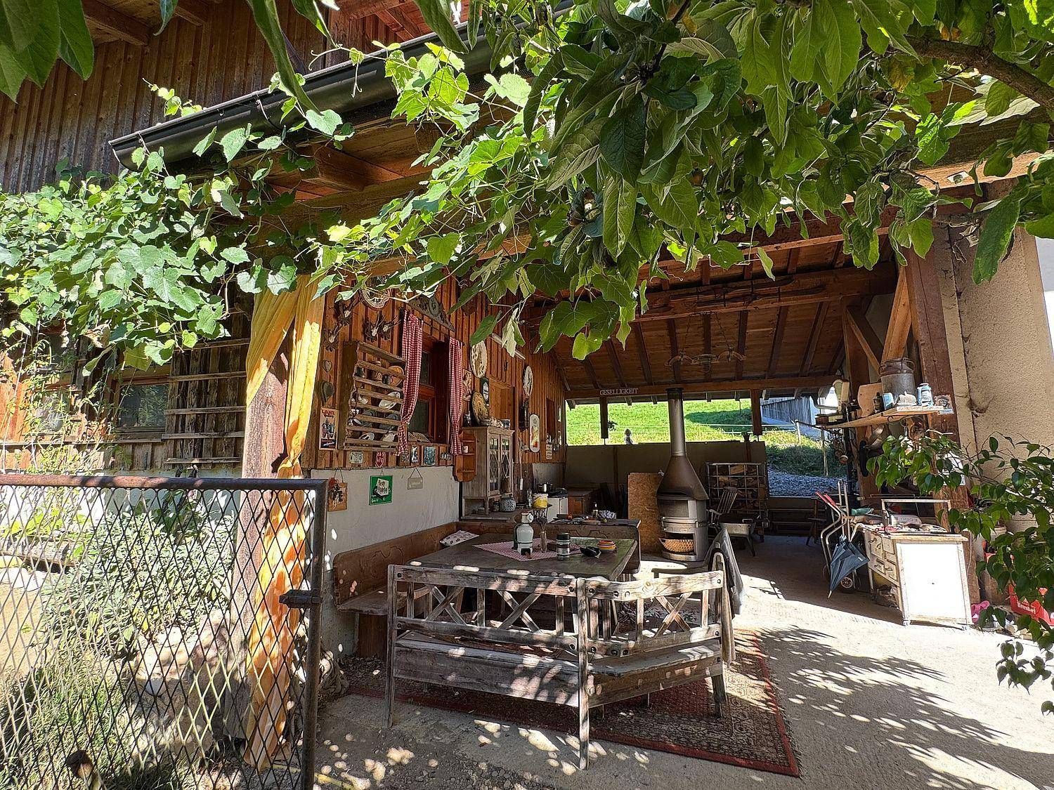 Rustikaler Essbereich im Freien unter einer überdachten Terrasse mit Holzbänken.