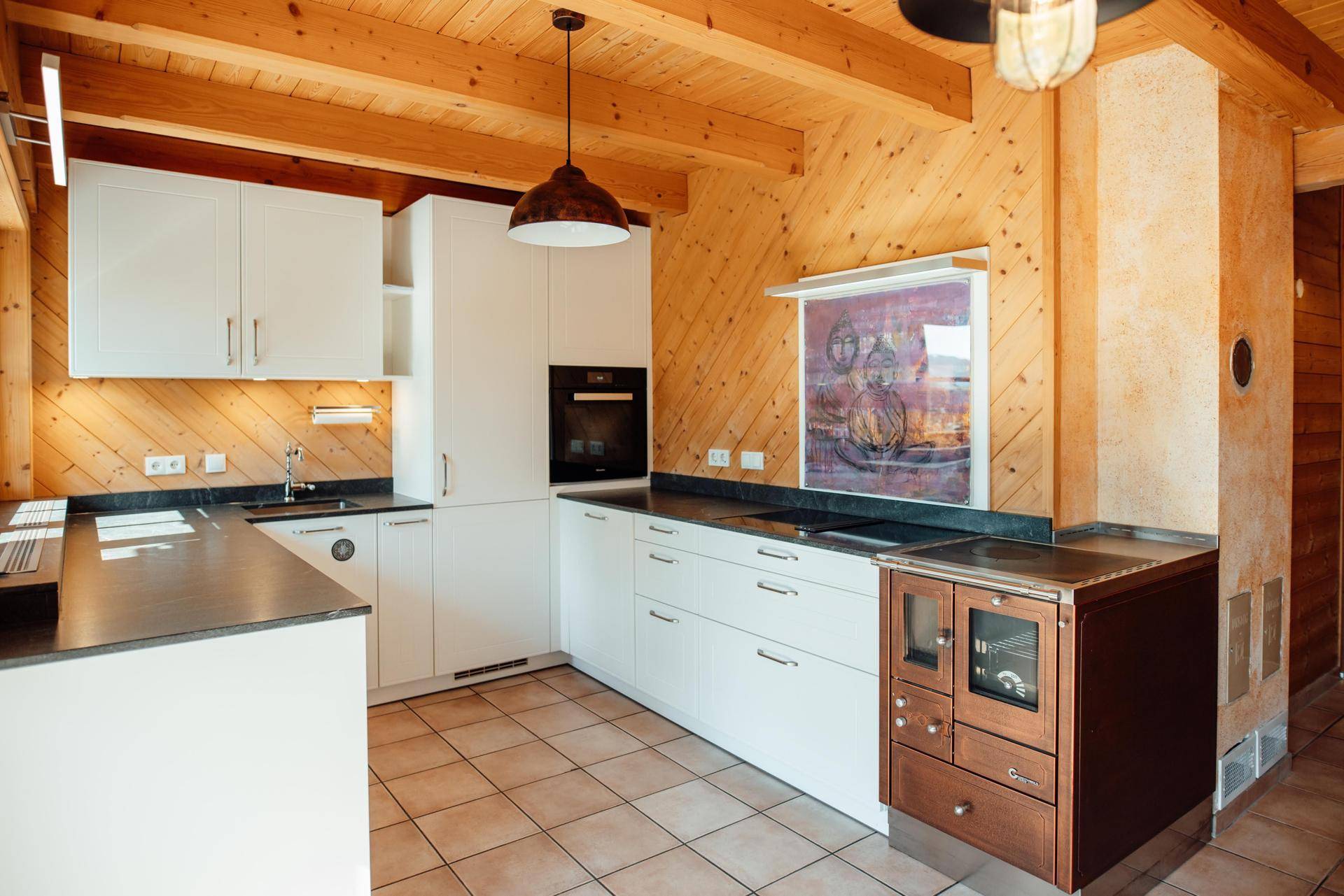 Gemütliche Küche im Landhausstil mit Holzwänden, Fliesenboden und traditionellem Holzofen.