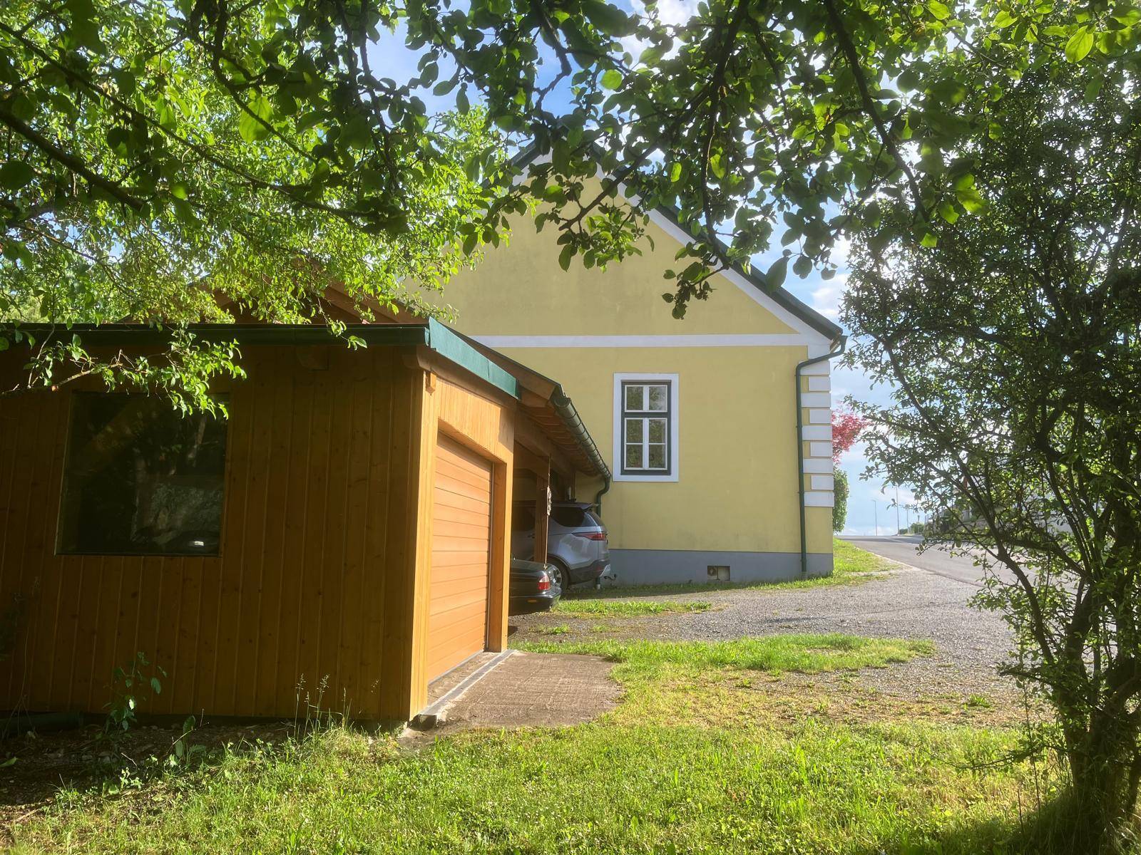 Gelbes Wohnhaus mit traditionellen Fenstern und einem praktischen Holzcarport für Fahrzeuge.