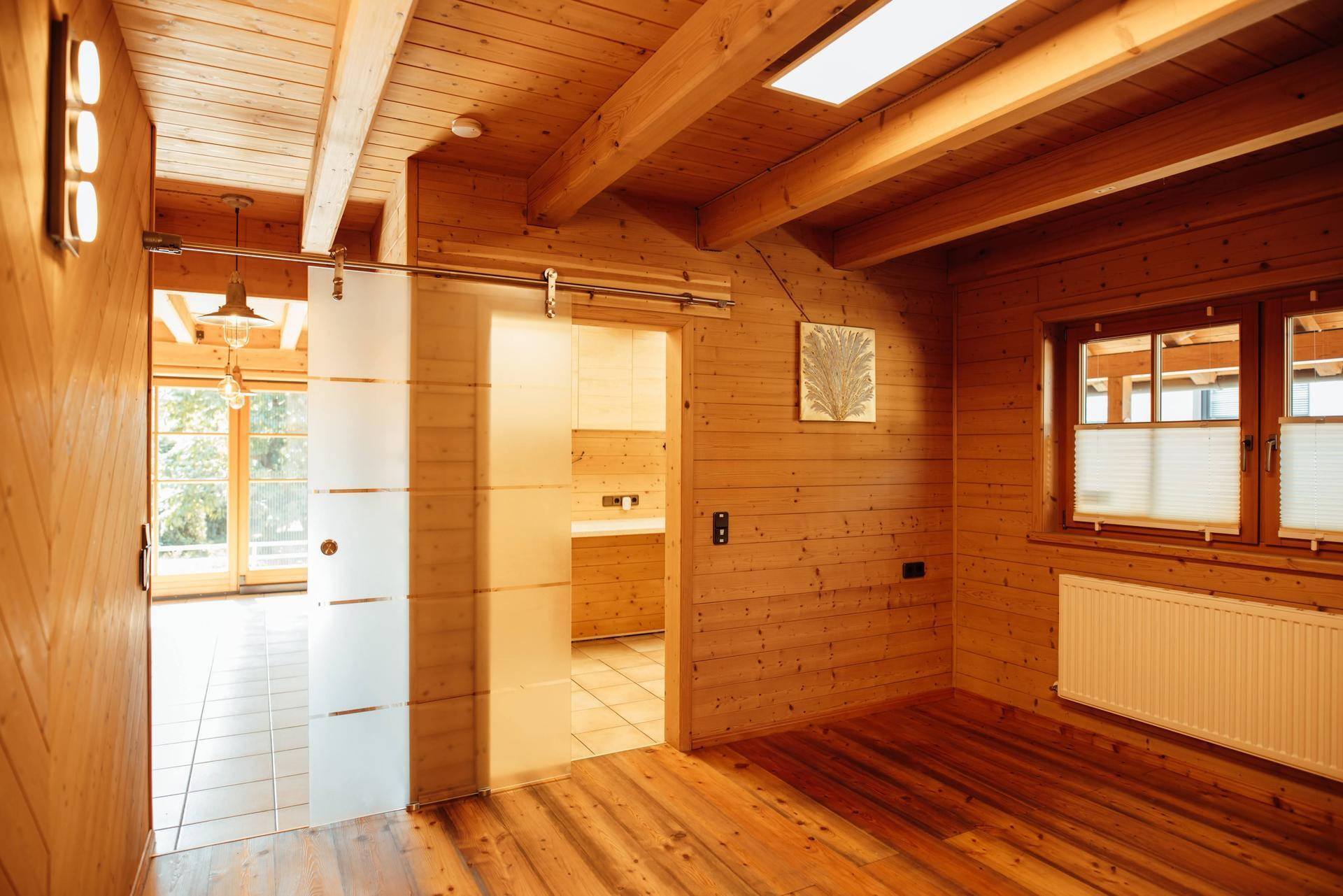Raum mit Holzboden, Holzvertäfelung und einer modernen Schiebetür aus Milchglas.