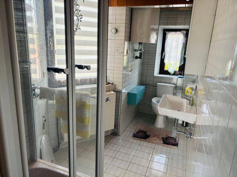 Gefliestes Badezimmer mit Duschkabine, WC, Waschbecken und Fenster für Tageslicht.
