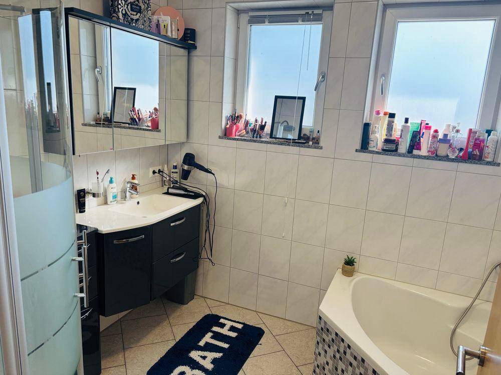 Helles Badezimmer mit Eckbadewanne, modernem Waschtisch und zwei Fenstern für Tageslicht.