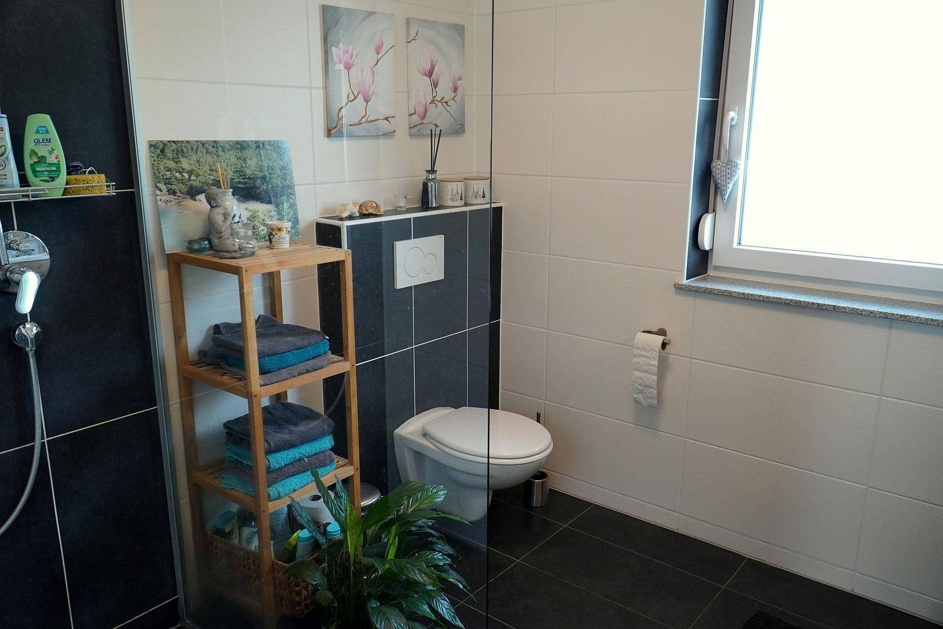 Modernes Badezimmer mit dunklen Bodenfliesen, weißer Wandverkleidung und Fenster.