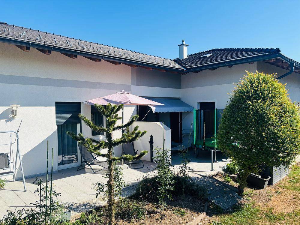 Geräumige Terrasse mit Sonnenschirm und Trampolin, umgeben von Bäumen und Sträuchern.