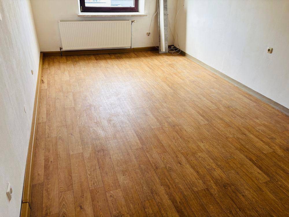 Leerer Raum mit Laminatboden, weiß gestrichenen Wänden und Heizkörper unter dem Fenster.