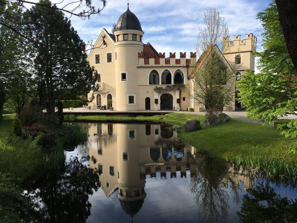 Historisch anmutendes Anwesen mit Zinnen und Turm, gespiegelt in einem ruhigen Teich.
