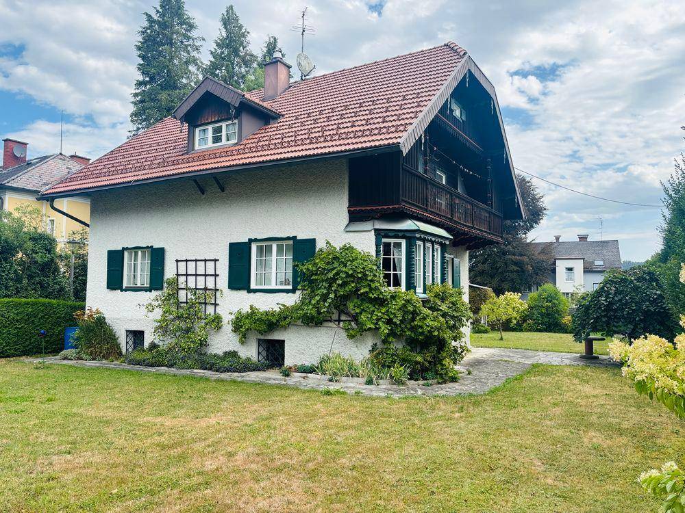 Freistehendes Haus mit großem Garten, traditionellem Holzbalkon und grünen Fensterläden.
