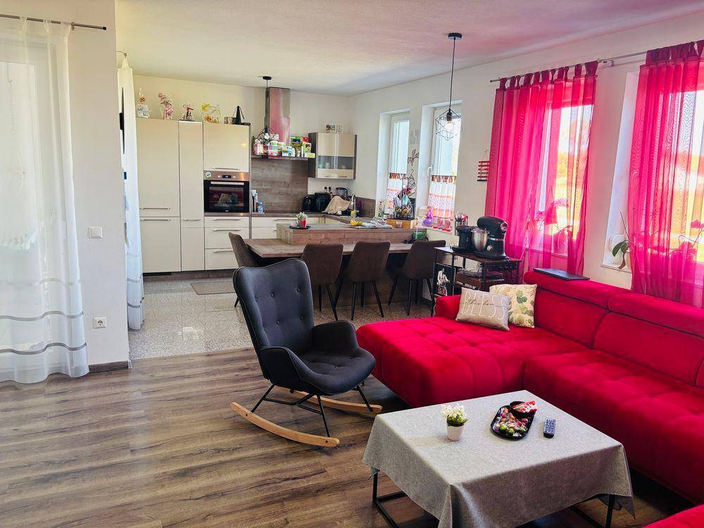 Offener Wohnbereich mit rotem Sofa, Essbereich und einer modernen Küche in hellen Farbtönen.