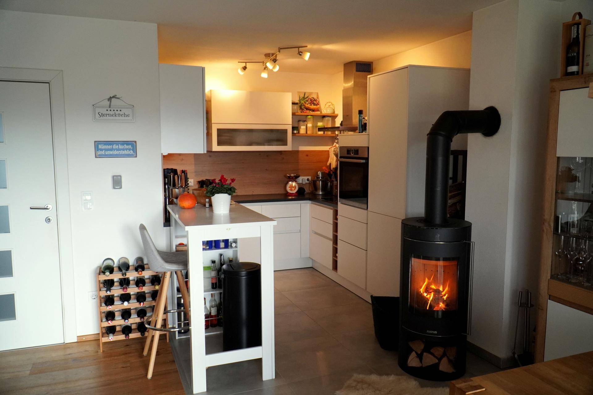 Moderne Küche mit weißer Einbauküche, Kochinsel und gemütlichem Holzofen.
