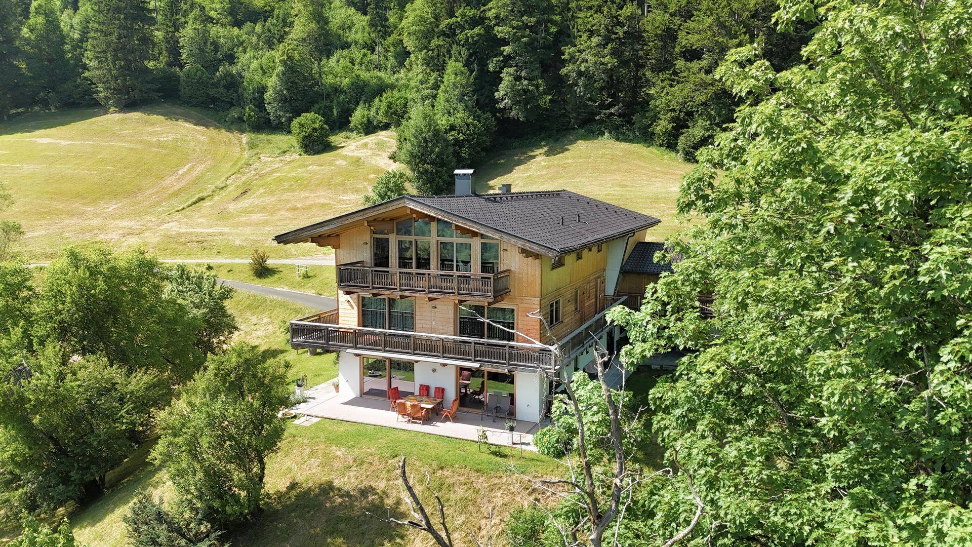 Panoramablick auf ein traditionelles Holzchalet mit großen Fenstern und mehreren Balkonen inmitten der Natur.