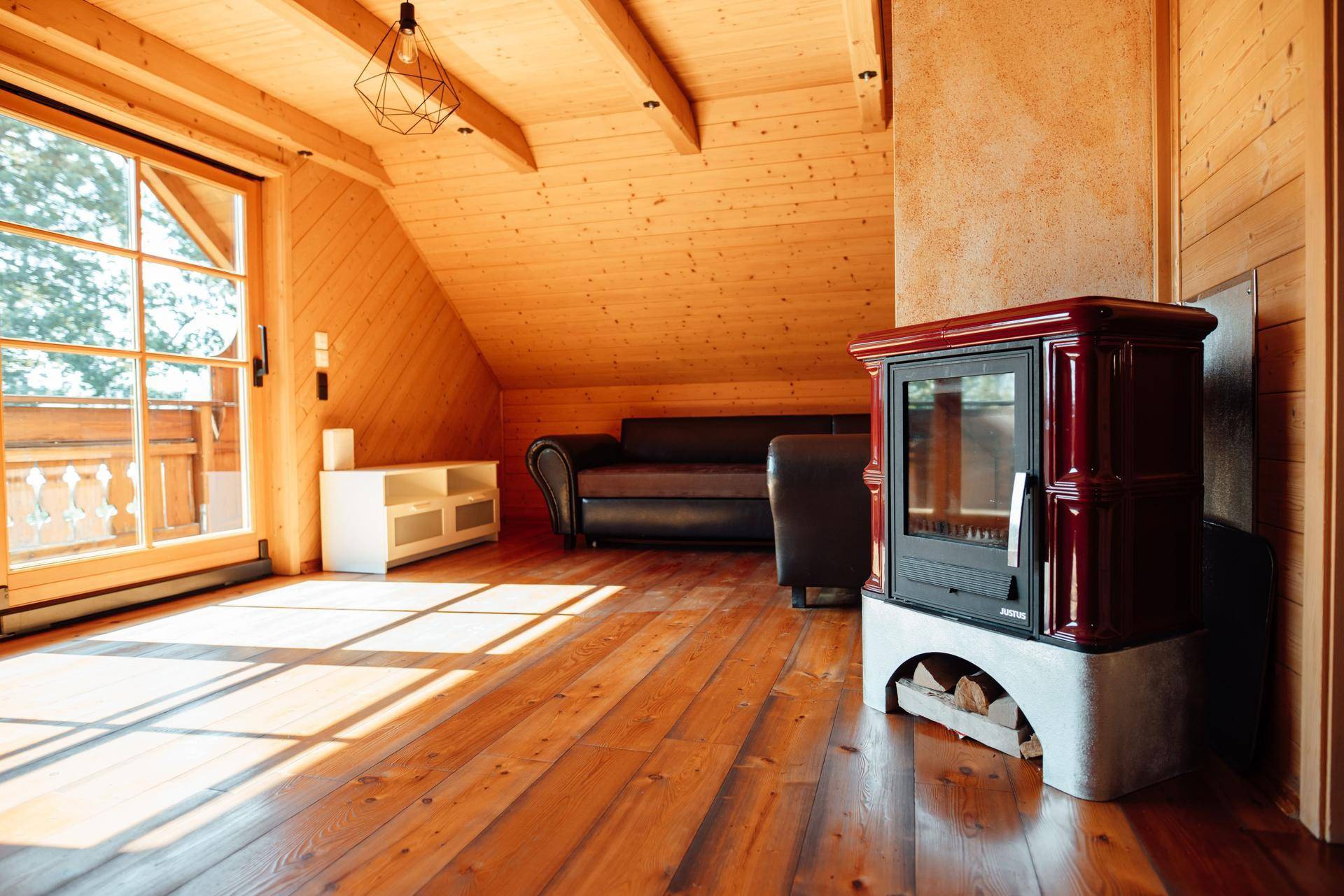 Gemütliches Wohnzimmer im Dachgeschoss mit Holzboden, Kaminofen und Zugang zum Balkon.