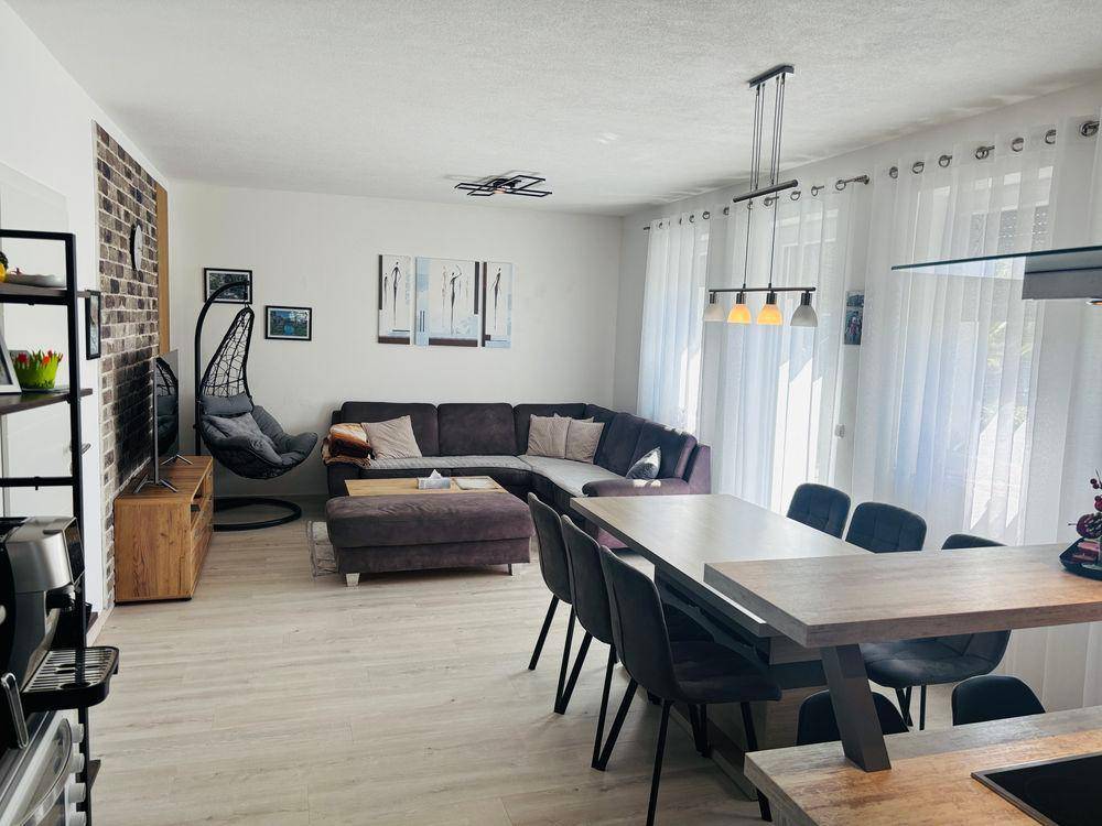 Heller, offener Wohn-Essbereich mit modernem Sofa, großem Esstisch und dekorativer Ziegelwand.