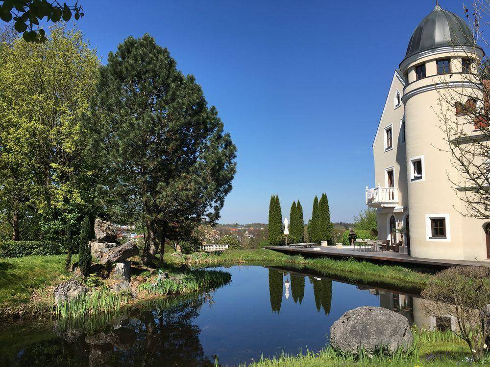 Teich mit Spiegelung des Anwesens und Holzterrasse unter klarem Himmel.