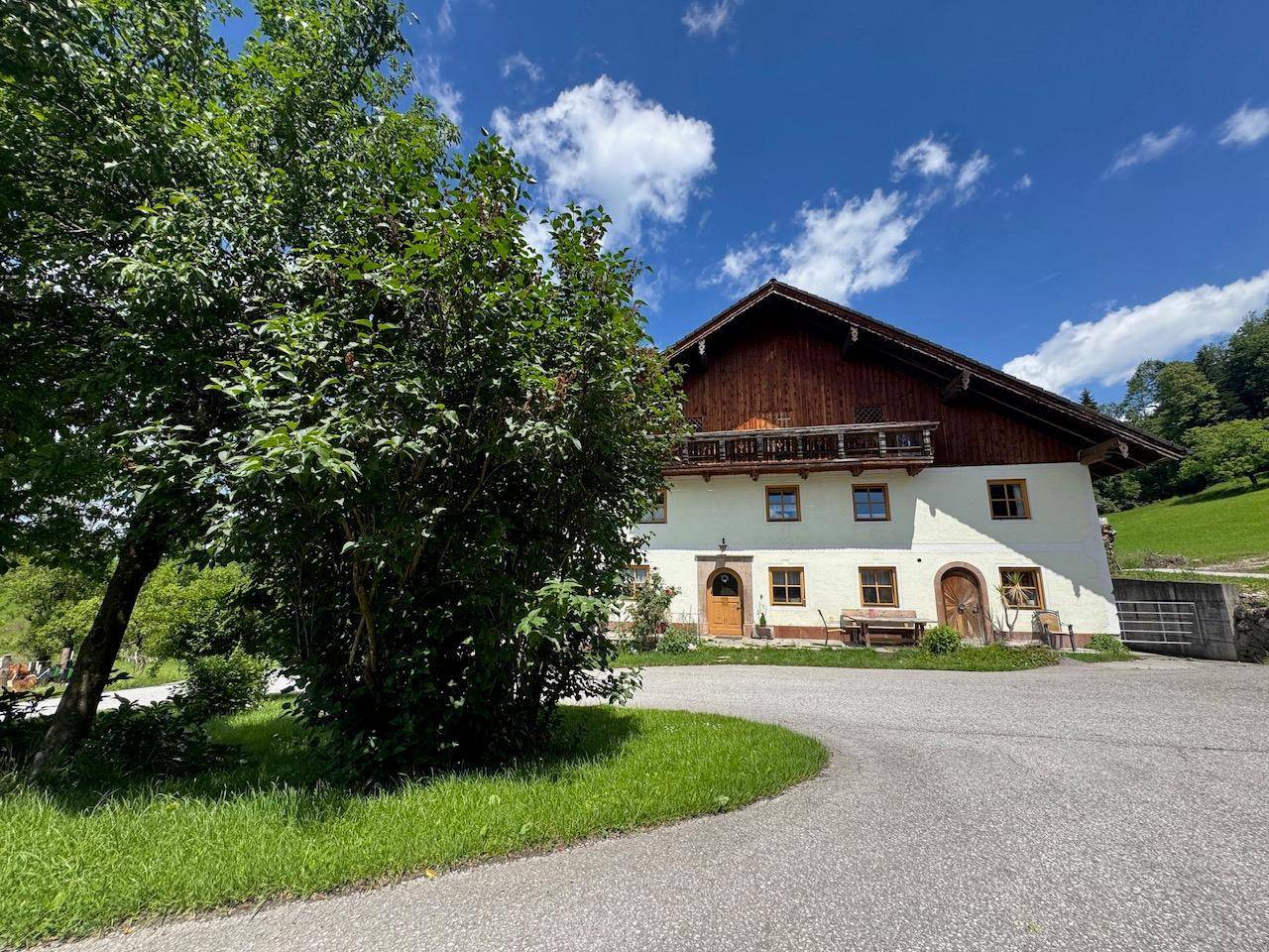 Charmantes Landhaus mit Holzbalkon und gepflegter Auffahrt, eingebettet in eine idyllische Landschaft.