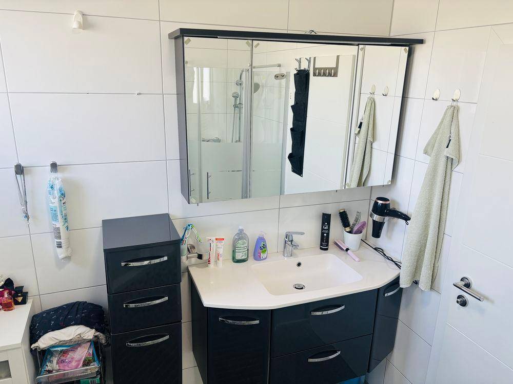 Badezimmer mit modernem Waschtisch, Spiegelschrank und Duschbereich, der sich im Spiegel widerspiegelt.
