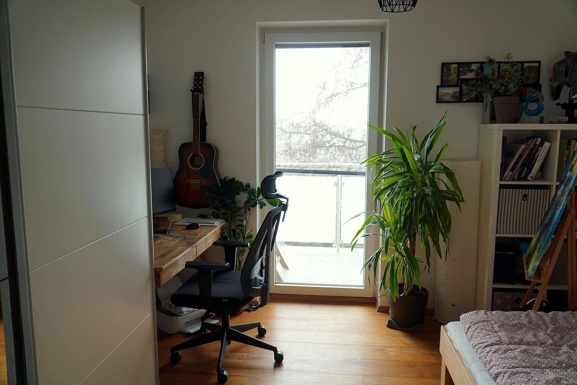 Helles Arbeitszimmer mit Schreibtisch, Pflanzen und Zugang zu einem französischen Balkon.