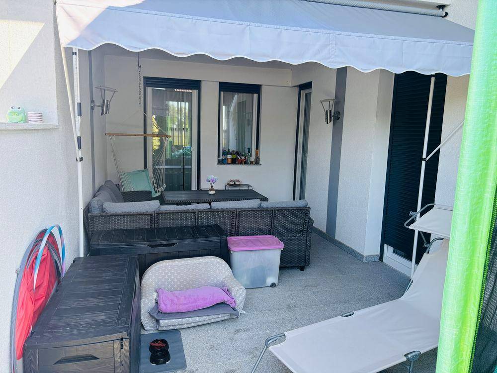 Überdachte Terrasse mit bequemen Lounge-Möbeln und praktischen Aufbewahrungsboxen für den Außenbereich.