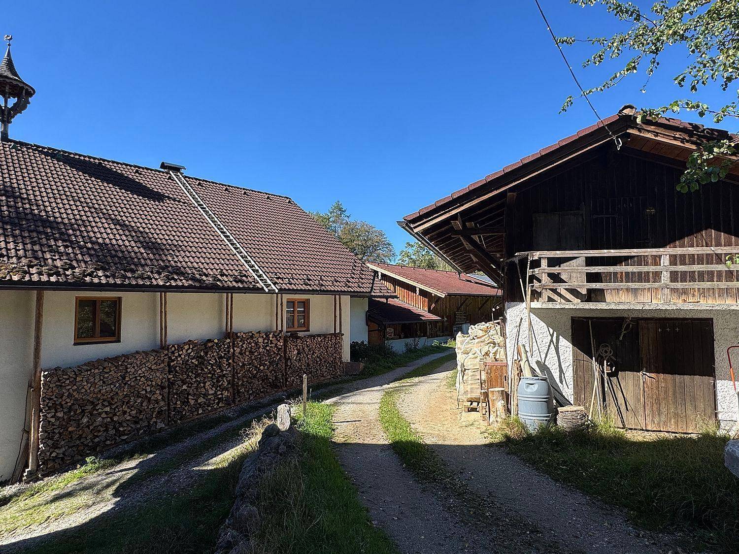 Traditionelle Hofgebäude mit Holzstapeln und einem Weg in ländlicher Umgebung.
