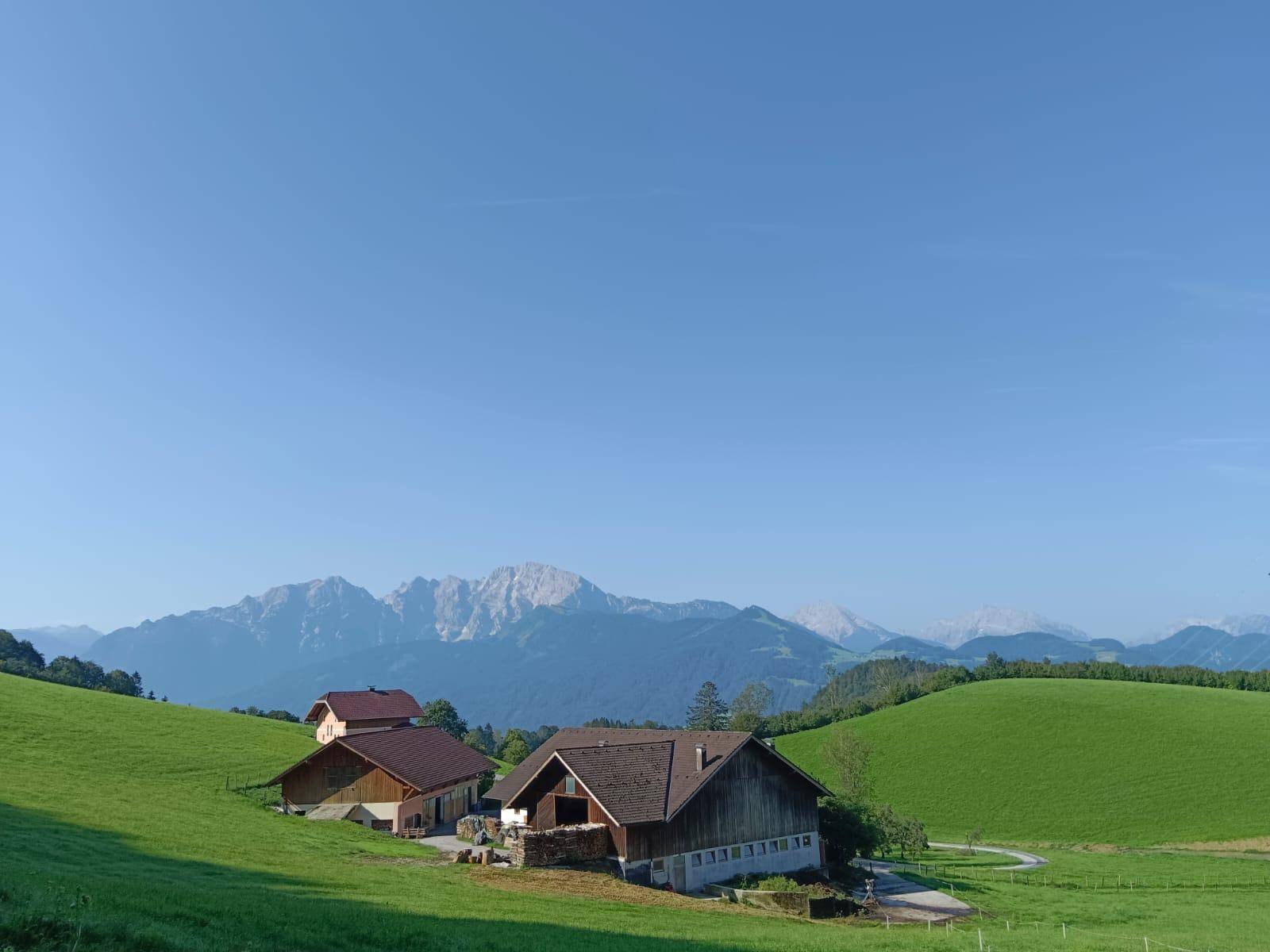 Malerische Landschaft mit grünen Hügeln und traditionellen Häusern, im Hintergrund majestätische Berge.