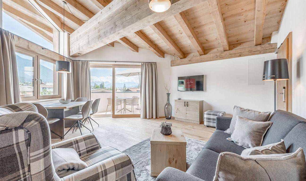 Heller Wohn- und Essbereich mit Holzbalkendecke, Parkettboden und Zugang zum Balkon.