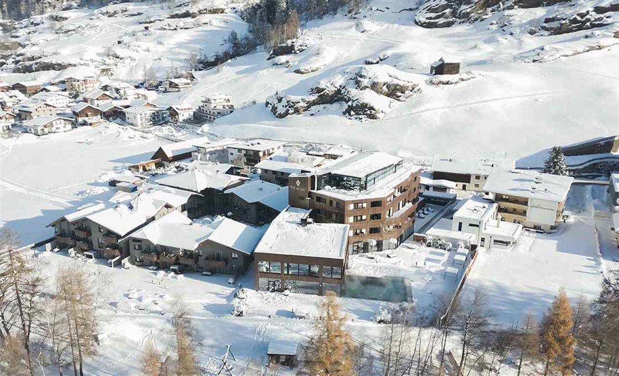 Winterliche Luftaufnahme des Hotelkomplexes eingebettet in eine verschneite Alpenlandschaft.