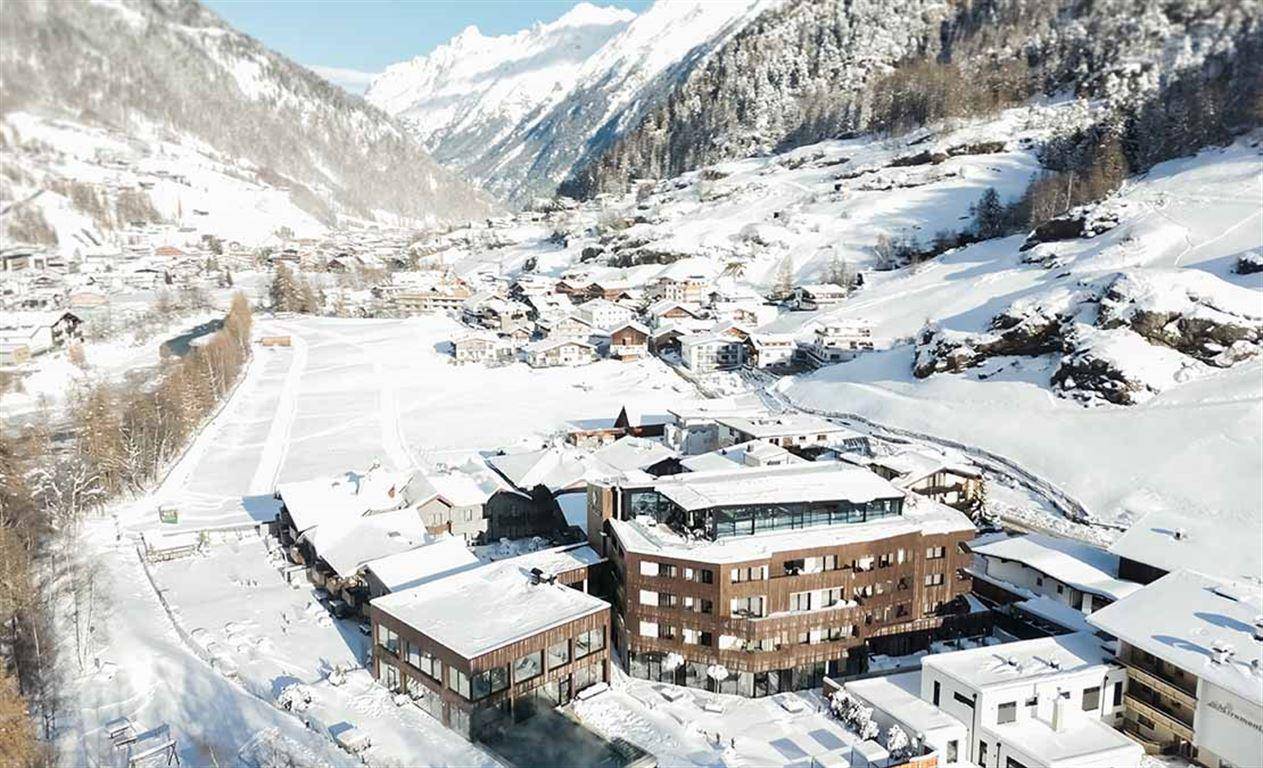 Weitläufige Luftaufnahme des verschneiten Dorfes und des Hotelgebäudes in den Alpen.