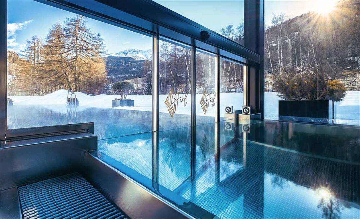 Innenpoolbereich mit großer Glasfassade und Panoramablick auf die verschneite Bergwelt.