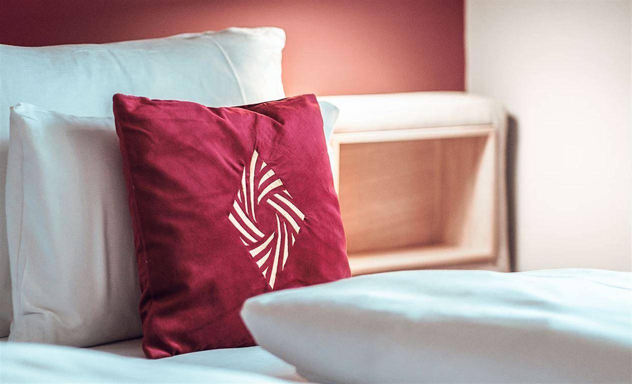 Nahaufnahme eines roten Kissens mit stilisiertem Logo auf dem Bett.
