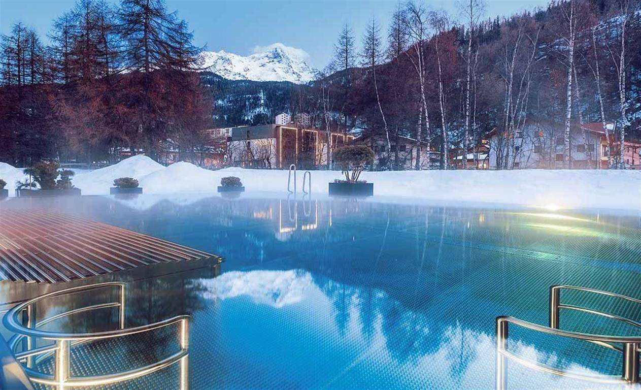Beheizter Außenpool in verschneiter Berglandschaft mit Blick auf die Alpen.