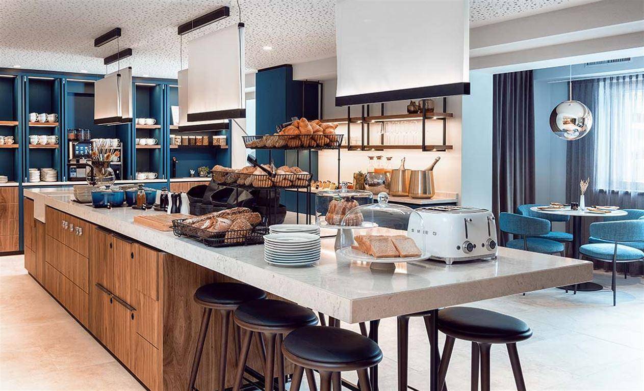 Reichhaltiges Frühstücksbuffet mit frischen Backwaren und modernen Küchengeräten.