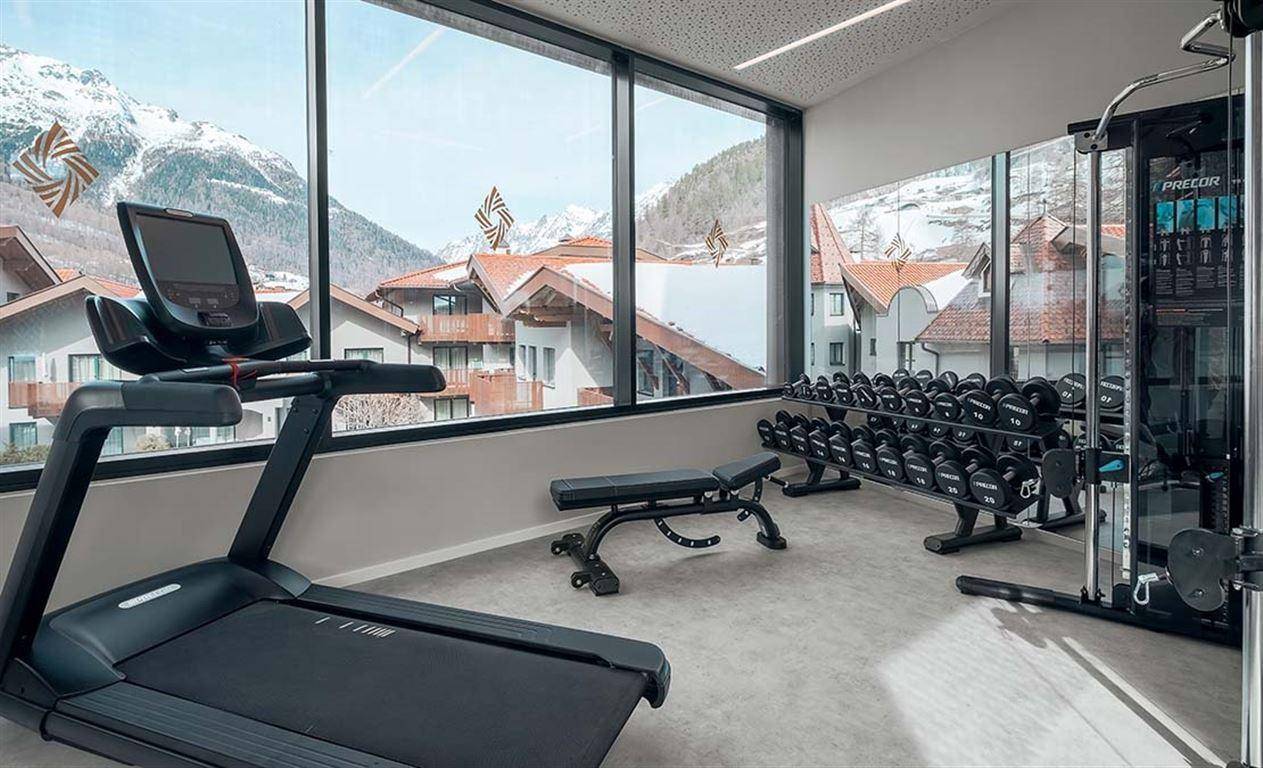 Moderner Fitnessraum mit Laufband, Hanteln und Panoramablick auf die Berglandschaft.