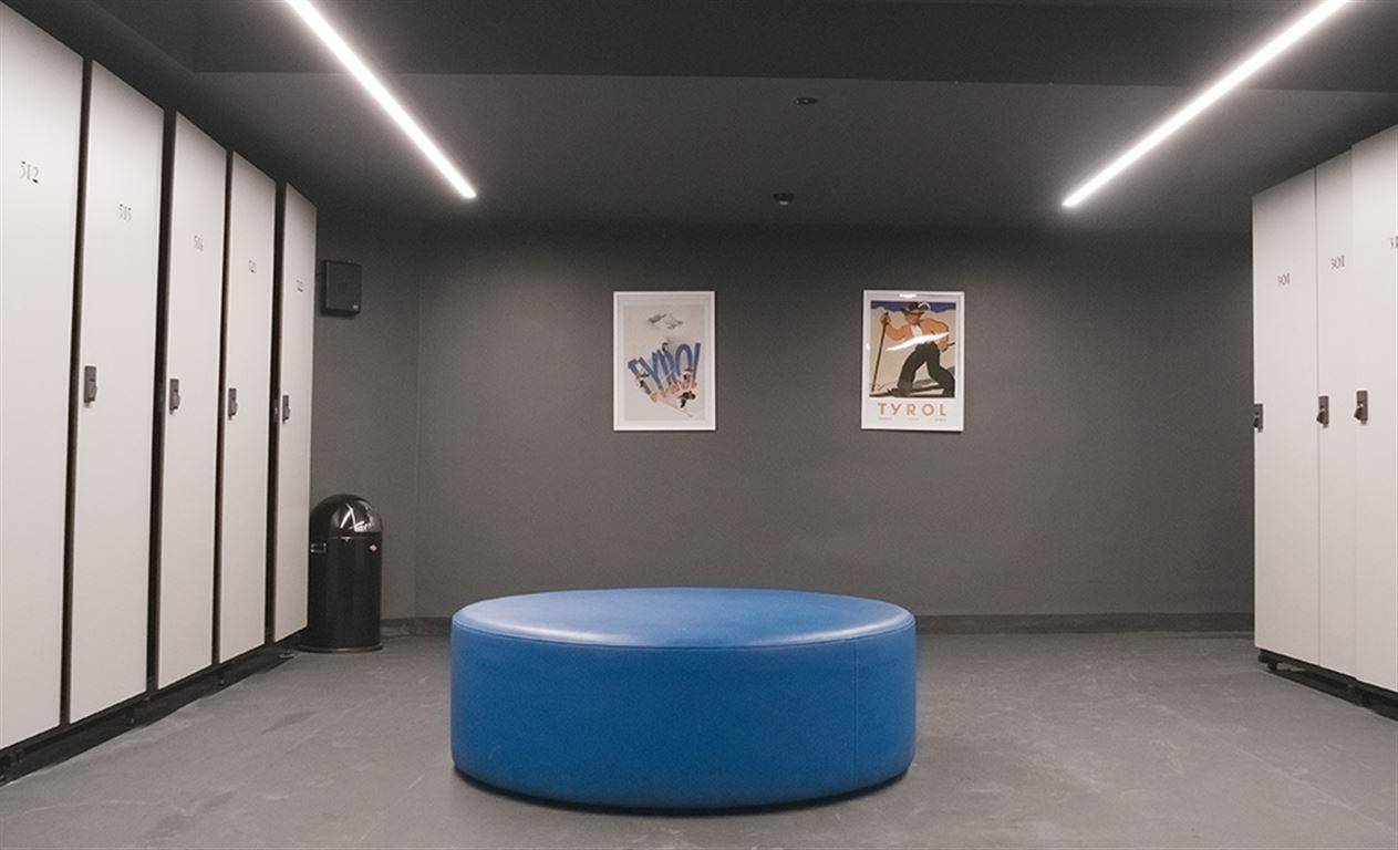 Umkleideraum mit weißen Spinden, blauer Sitzbank und minimalistischer Beleuchtung.