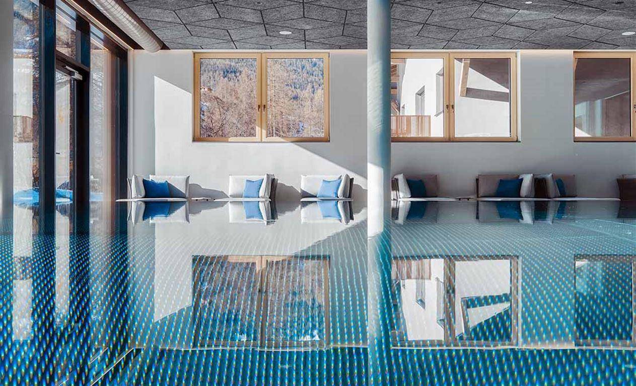 Innenpoolbereich mit bequemen Liegen und großen Fenstern, die die Umgebung widerspiegeln.