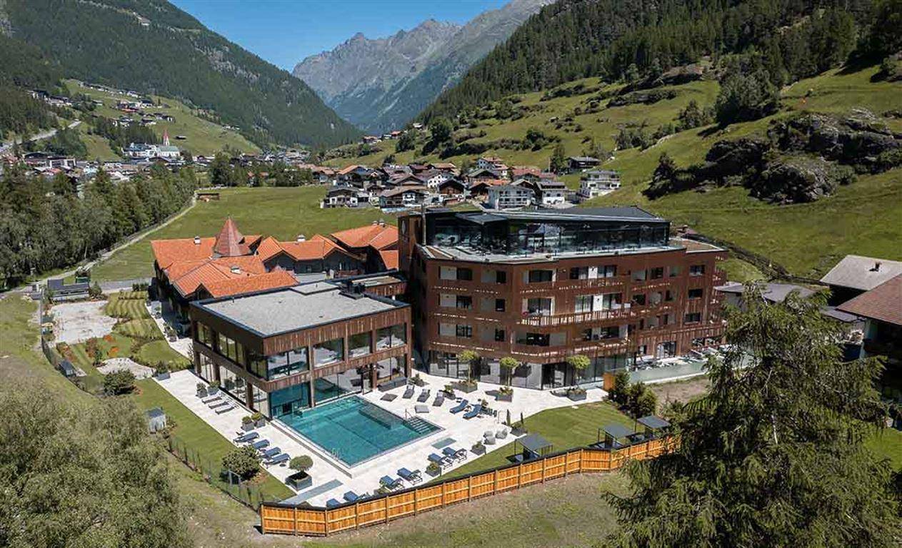 Sommerliche Luftaufnahme des Gebäudekomplexes mit Außenpool und grüner Berglandschaft.