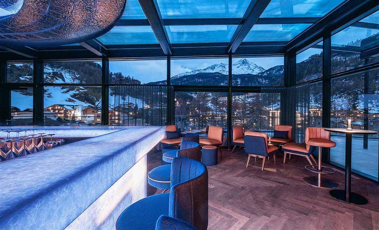 Elegante Bar und Lounge mit Glasdach und Panoramablick auf die verschneiten Berge.