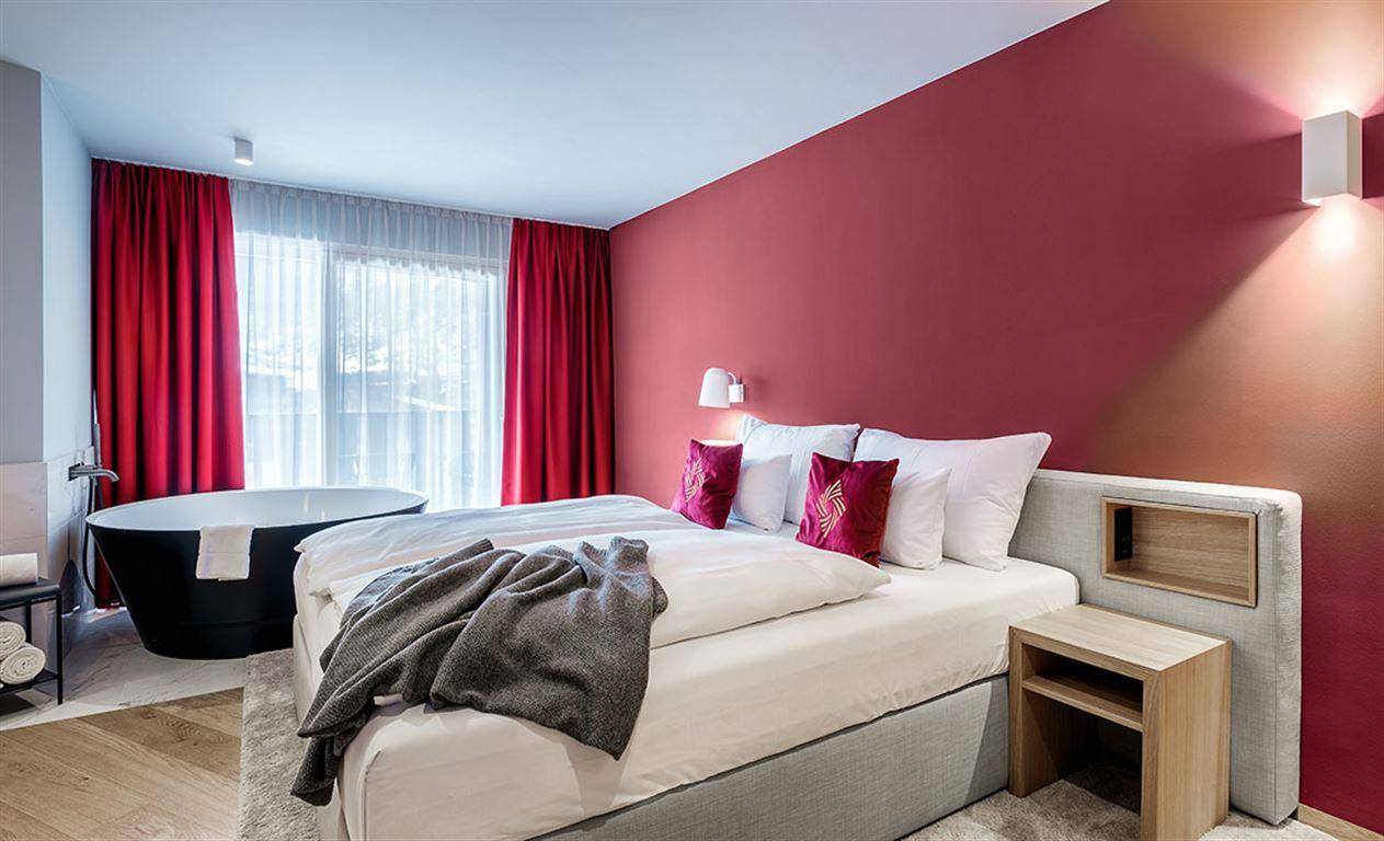 Modernes Schlafzimmer mit freistehender Badewanne und roter Akzentwand.