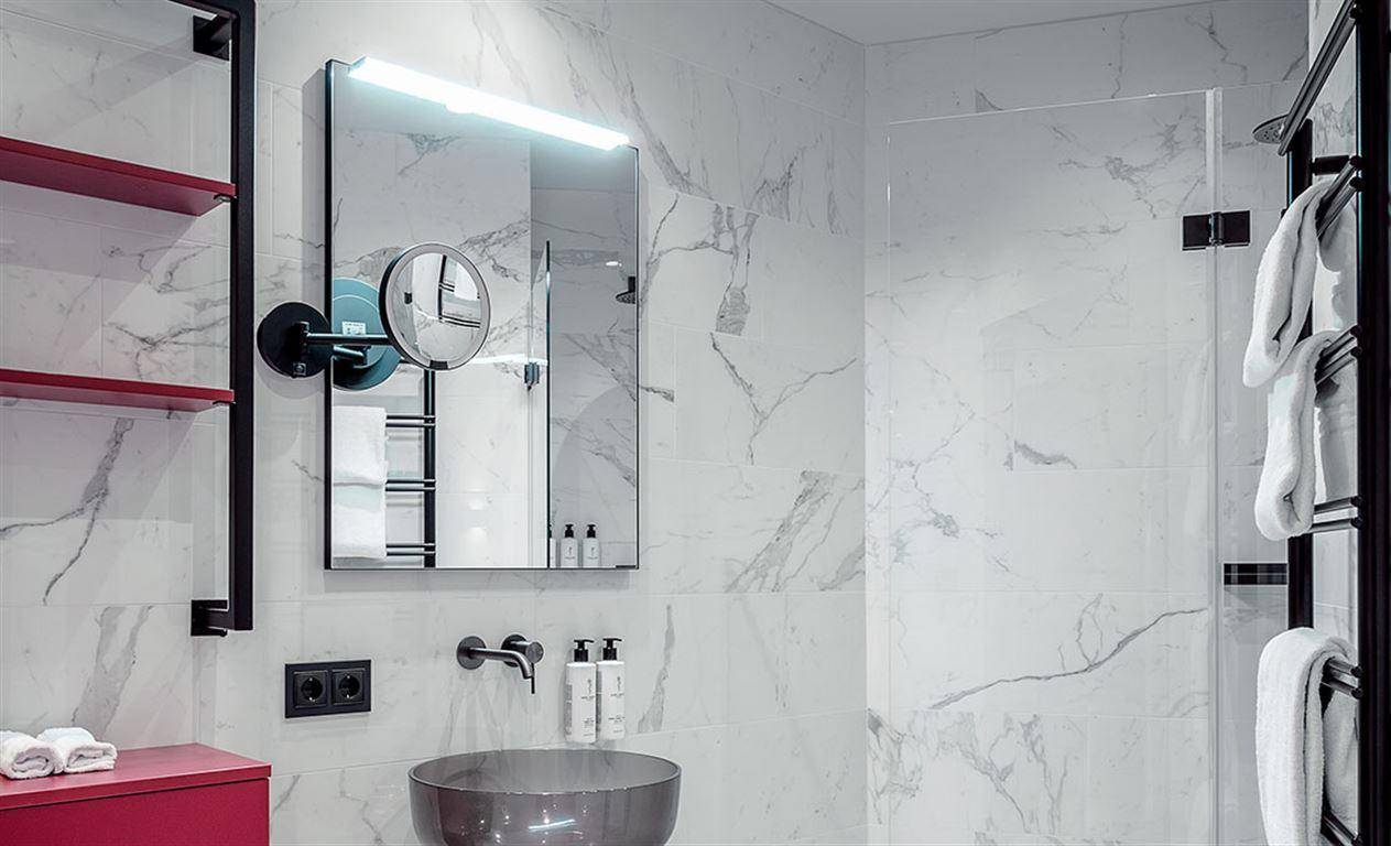 Elegantes Badezimmer mit Marmorwänden, modernem Waschbecken und rahmenloser Glasdusche.