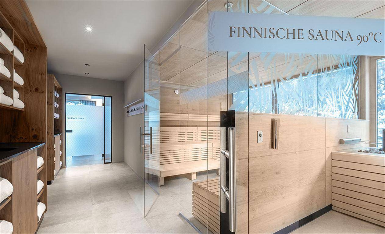 Moderne finnische Sauna mit Holzbänken und Glasfront in einem luxuriösen Wellnessbereich.