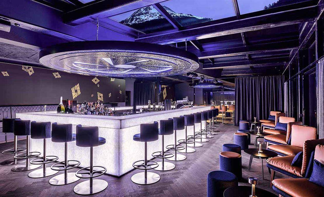 Exklusive Bar mit leuchtender Theke, hohen Hockern und stilvoller Deckenbeleuchtung.