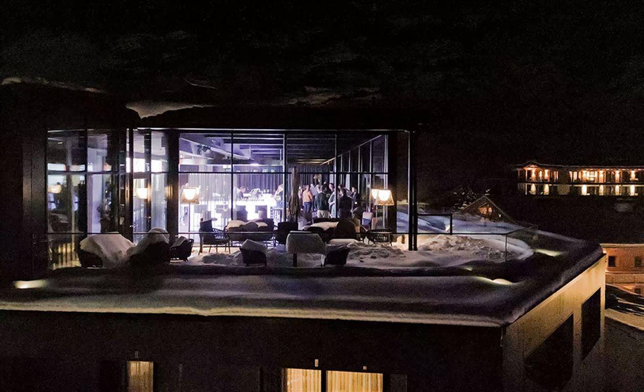 Beleuchtete Dachterrasse mit Sitzgelegenheiten und Blick auf die verschneite Umgebung bei Nacht.