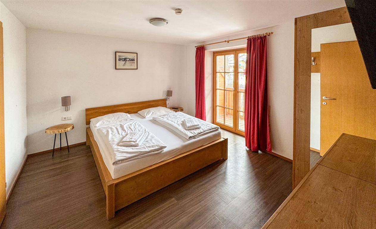 Gemütliches Schlafzimmer mit Doppelbett, Holzboden und Zugang zu einem kleinen Balkon.